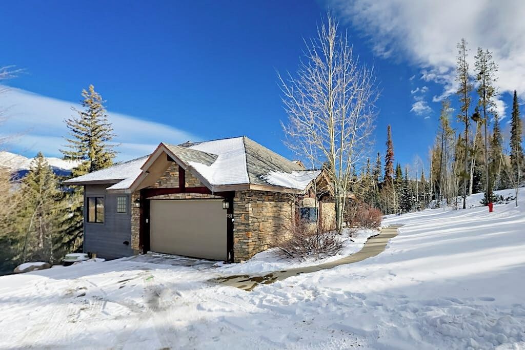 A house with a garage, surrounded by snow-covered ground and trees.