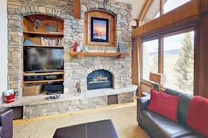 A stone fireplace with a television and bookshelves, a sofa, and a window with a view. - Well-appointed home with home theater, radiant heat & private hot tub (Fraser)