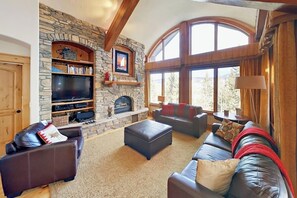 A cozy living room with a stone fireplace, leather sofas, a flat-screen TV, and large windows. - Well-appointed home with home theater, radiant heat & private hot tub (Fraser)