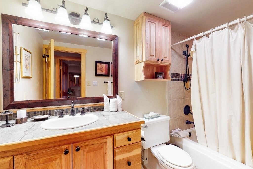 A bathroom with a wooden vanity, a large mirror, a toilet, and a shower curtain.
