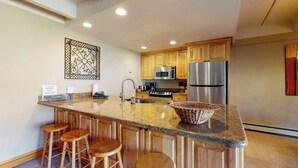 Una cocina con armarios de madera, un refrigerador de acero inoxidable, un microondas y una encimera de granito.