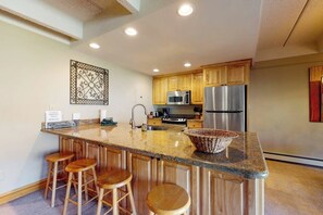 A kitchen with wooden cabinets, a stainless steel refrigerator, a microwave, and a granite countertop. - Charming mountain condo w/Vail Pass views, gas fireplace, deck, & shared hot tub (Copper Mountain)