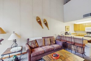 A living room with a sofa, a coffee table, a lamp, and a kitchen area with a bar.