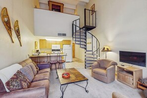 A living room with a sofa, armchair, coffee table, TV, and a spiral staircase leading to an upper level.
