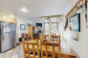 A kitchen with a built-in refrigerator, wooden dining table, chairs, and a spiral staircase.
