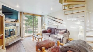 A modern living room with a fireplace, a sofa, a coffee table, and a staircase. - Dog-friendly, ski condo with golf course views, balcony, hot tub & sauna (Copper Mountain)