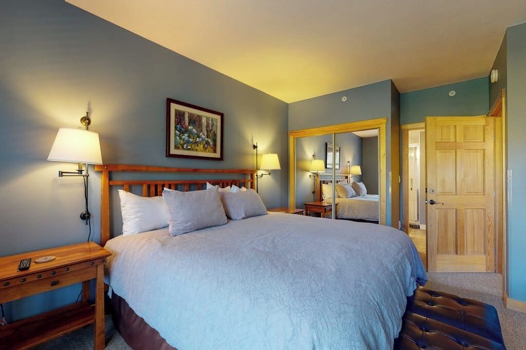 A bedroom with a bed, bedside tables, a mirror, and a door.