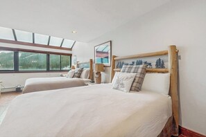 Ein Zimmer mit zwei Betten, einem Oberlicht, einem Gemälde und Blick auf Bäume.