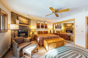 Ein Schlafzimmer mit Kamin aus Stein, einem Bett mit Kopfteil, einer hölzernen Bank, einem Deckenventilator und einem großen Spiegel.