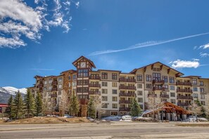 A multi-story hotel with a prominent clock tower, balconies, and a ski resort backdrop. - Spacious & Bright Condo W/ Shared Pool, Easy Ski Access & Free WiFi (Copper Mountain)