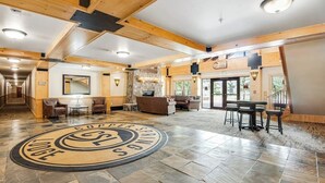 Eine großzügige Lobby mit einem zentralen, runden Emblem, Holzbalken und einer Sitzecke mit Tischen und Stühlen.