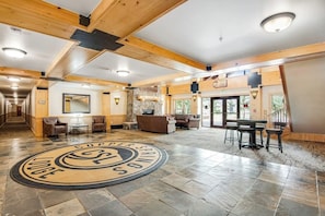 Eine großzügige Lobby mit einem zentralen, runden Emblem, Holzbalken und einer Sitzecke mit Tischen und Stühlen.