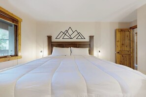 Ein Schlafzimmer mit einem großen Bett, einem hölzernen Kopfteil, einem Kunstwerk mit Bergmotiven an der Wand und einer Holztür.