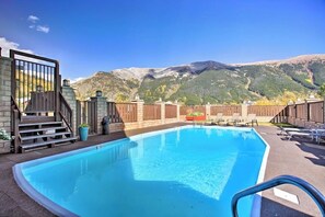 Ein rechteckiger Pool mit Holzterrasse, einem Metallgitter und Blick auf Berge.