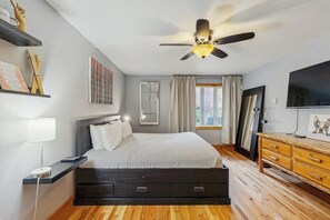 A bedroom with a bed, a ceiling fan, a TV, a wooden dresser, and a window with curtains. - Ground-Floor Condo with WiFi, Laundry & Prime Location - Walk Everywhere (Frisco)
