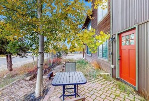 A patio with a table and chairs, a red door, and a tree with yellow leaves. - Ground-Floor Condo with WiFi, Laundry & Prime Location - Walk Everywhere (Frisco)
