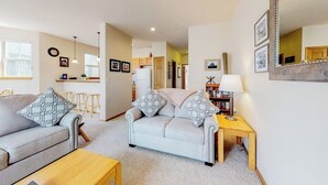 A living room with a sofa, a coffee table, a side table, and a lamp. There are framed pictures on the wall and a clock.