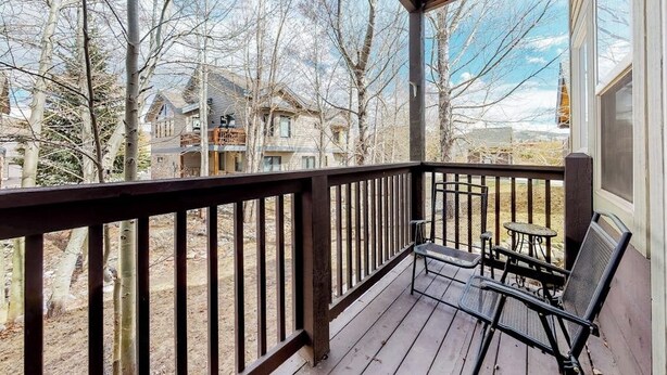A wooden deck with a railing, two chairs, and a small table.