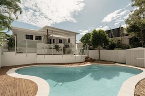 Ein modernes Haus mit Schwimmbad, umgeben von einer Holzterrasse und einem weißen Zaun.