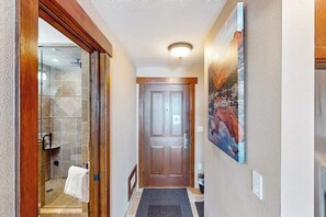 Un couloir avec une douche en verre, une porte en bois et un tableau accroché au mur.