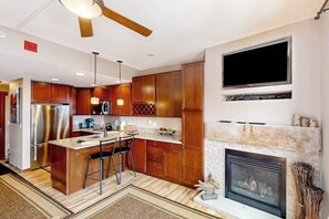 Eine moderne Küche mit Holzschränken, einem Edelstahlkühlschrank, einer integrierten Kücheninsel mit Barhocker, einem Flachbildfernseher und einem Kamin.