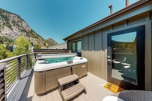 Ein Whirlpool auf einer Terrasse mit Blick auf die Berge, einer Glastür und einer Holzbank.