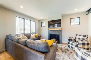 Ein Wohnzimmer mit grauem Sofa, Kamin, Fernseher und einem gemusterten Sessel.