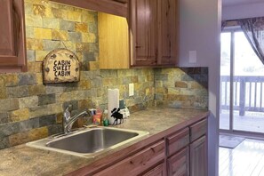 A kitchen with a stone backsplash, wooden cabinets, a sink, and a sign that reads 'CABIN SWEET CABIN.' - Ground-Floor, All-Seasons Condo with Shaded Deck and Gas Fireplace (Fraser)