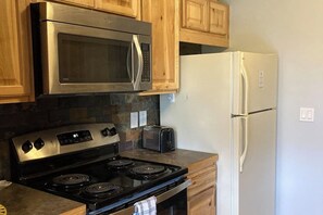 A kitchen with stainless steel appliances, wooden cabinets, a toaster, and a refrigerator. - Ground-Floor, All-Seasons Condo with Shaded Deck and Gas Fireplace (Fraser)