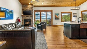 A spacious living area with a fireplace, a sofa, a dining area, and a kitchen. - Large mountain home with epic views, hot tub, &  gas fireplace (Grand Lake)