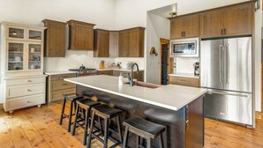 A kitchen with wooden cabinets, a stainless steel refrigerator, a microwave, and a large island with stools. - Large mountain home with epic views, hot tub, &  gas fireplace (Grand Lake)
