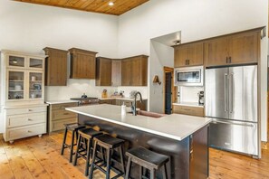 A kitchen with wooden cabinets, a stainless steel refrigerator, a microwave, and a large island with stools. - Large mountain home with epic views, hot tub, & gas fireplace (Grand Lake)