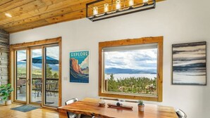 A wooden dining table with chairs, a poster, and a view through large windows. - Large mountain home with epic views, hot tub, &  gas fireplace (Grand Lake)