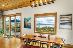 A wooden dining table with chairs, a poster, and a view through large windows. - Large mountain home with epic views, hot tub, & gas fireplace (Grand Lake)