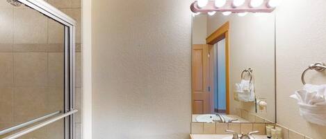 A bathroom with a shower, toilet, sink, and vanity mirror with lights.
