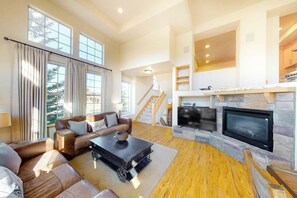 Ein geräumiges Wohnzimmer mit Kamin, Ledersofas, einem Couchtisch und einer Treppe, die in eine obere Etage führt.