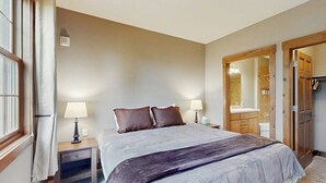 Quarto com cama, abajures, mesa de cabeceira, espelho e porta de madeira.