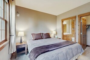 Ein Schlafzimmer mit Bett, Nachttischlampen, einem Nachttisch, einem Spiegel und einer Holztür.