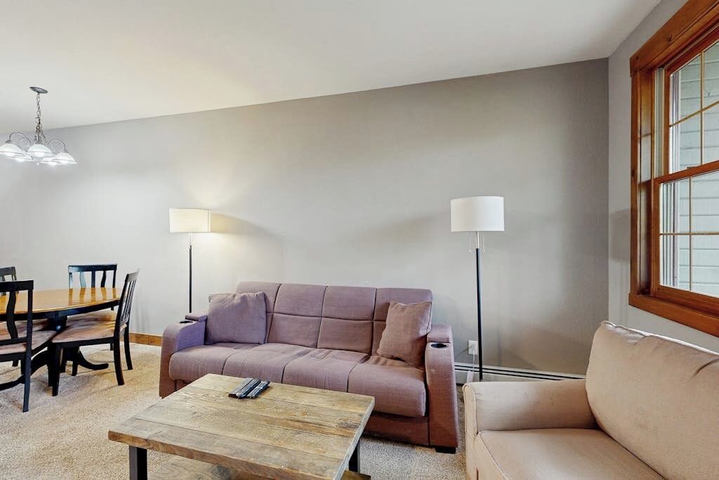 Ein Wohnzimmer mit einer Couch, einem Couchtisch, einem Esstisch mit Stühlen und zwei Stehlampen.