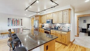 Una cocina moderna con gabinetes de madera, encimera de granito y una isla central con taburetes de bar.