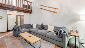 Una sala de estar moderna con un sofá seccional, una mesa de centro de madera y una escalera que conduce a un nivel superior.