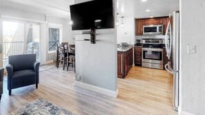 Een moderne keuken met een flatscreen televisie, houten kastjes, roestvrijstalen apparatuur en een eethoek met een barstoel.
