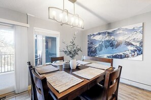 A dining area with a wooden table, chairs, a chandelier, a vase with plants, and a large mountain landscape painting on the wall. - Modern Waterfront Condo w/ Mountain View, W/D, & High Speed WiFi - Near Skiing (Frisco)