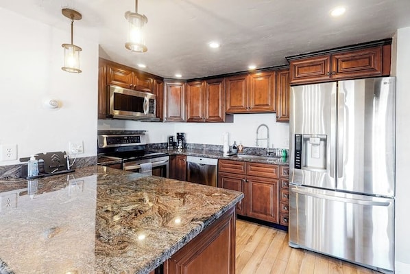 A kitchen with wooden cabinets, stainless steel appliances, granite countertops, and pendant lighting. - Modern Waterfront Condo w/ Mountain View, W/D, & High Speed WiFi - Near Skiing (Frisco)