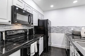 A modern kitchen with white cabinets, a black refrigerator, a stove, and a microwave. - Mountain-view townhome with balcony, gas fireplace, WiFi, & W/D - great location (Frisco)