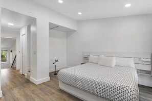 A modern bedroom with a large bed, white walls, and a wooden floor. - Mountain-view townhome with balcony, gas fireplace, WiFi, & W/D - great location (Frisco)