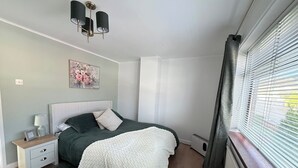 Et soveværelse med seng, sengebord, lampe, billedramme og et vindue med persienner.