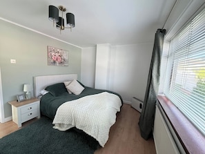 A bedroom with a bed, bedside table, lamp, picture frame, and a window with blinds. - 3BD Cozy Family Retreat for 5 (Belfast)