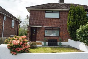 A two-story brick house with a front door, a window, and a small bench. - 3BD Cozy Family Retreat for 5 (Belfast)