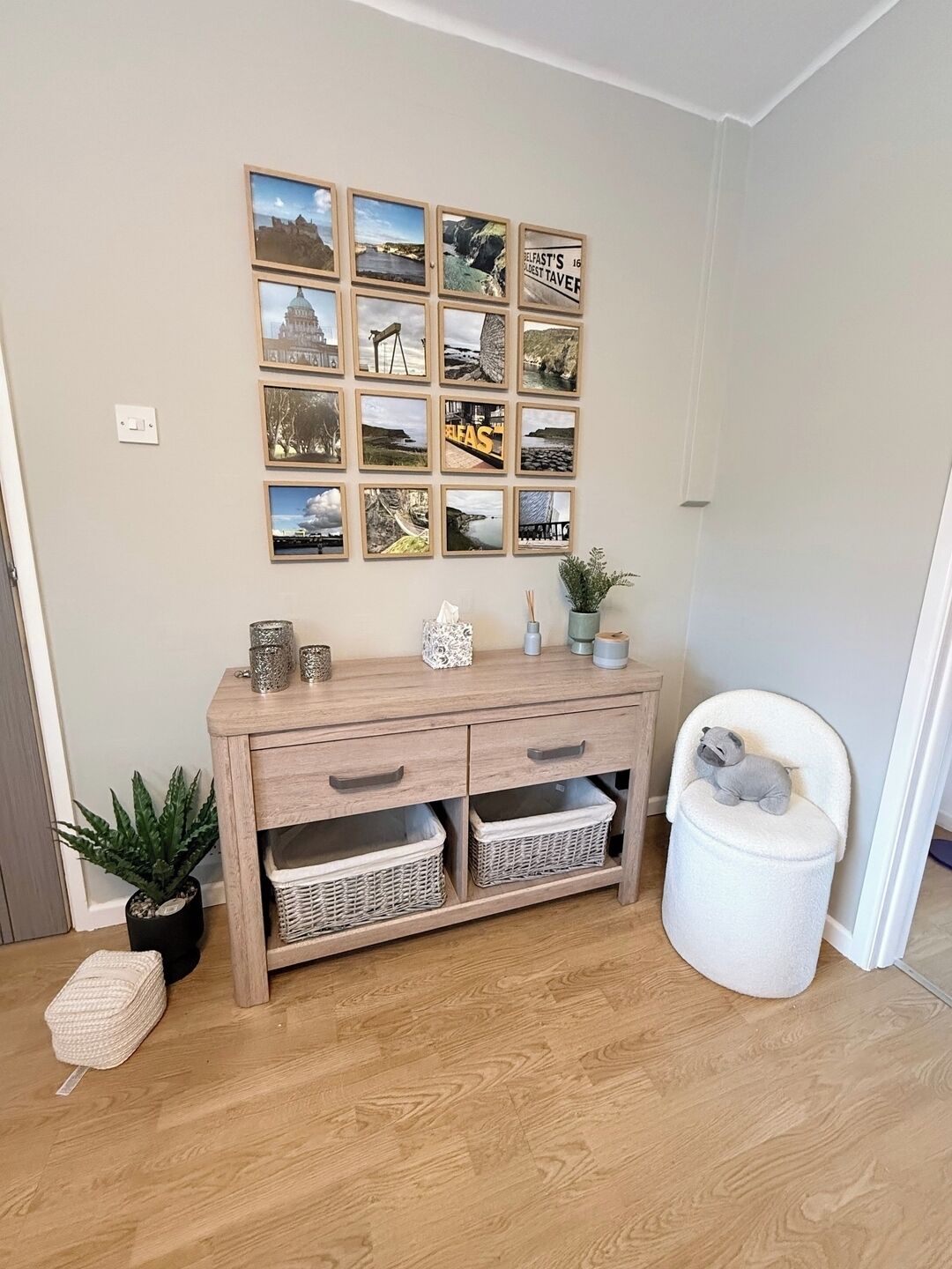 A room with a wooden console table, wicker baskets, a small potted plant, a decorative item, and a framed collage on the wall.